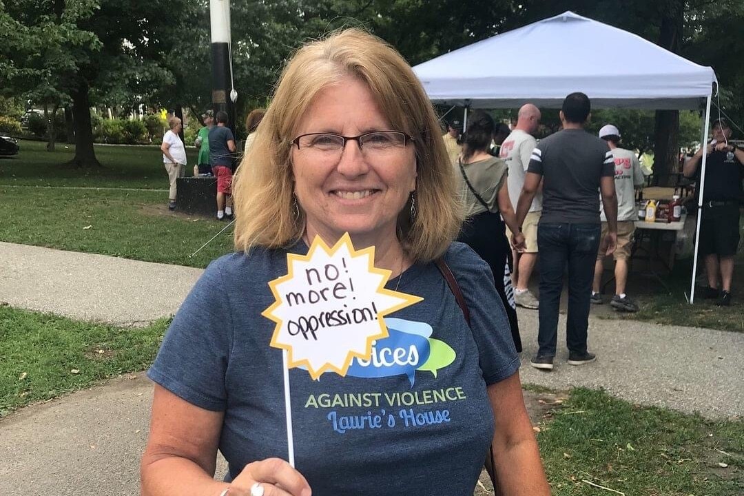 Kris Lukens, smiling, holding sign that reads "no more opression"